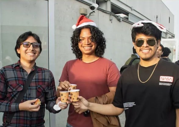 Tres asistentes con gorro navideño brindan con sus vasos de chocolate