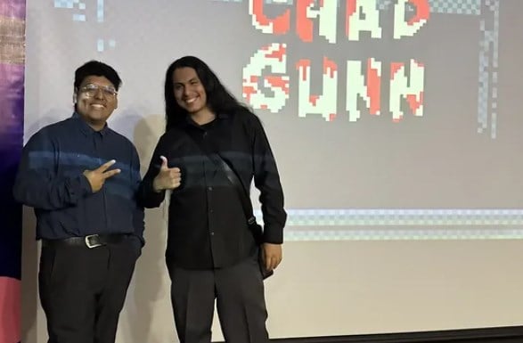 Dos desarrolladores posan ante la pantalla con el logotipo de Chad Gunn
