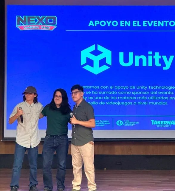 Tres organizadores de Takernal Community en el escenario, ante la diapositiva del apoyo de Unity